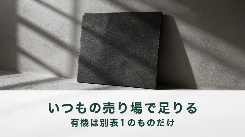 窓の格子の影が落ちる灰白色の粉の面に黒い焼き締めの陶板が一枚立ててある