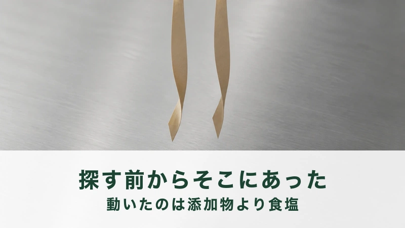 ステンレスの板の前にクラフト紙の細い帯が二本上から吊り下がっている