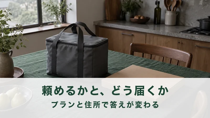 曇りの日の台所で、深緑のクロスに保冷バッグと平たい段ボール箱が並ぶ