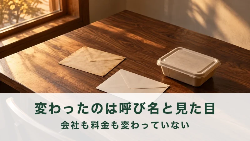 午後の書斎の机に、古い封筒と新しい封筒、ふた付きの惣菜容器が並ぶ