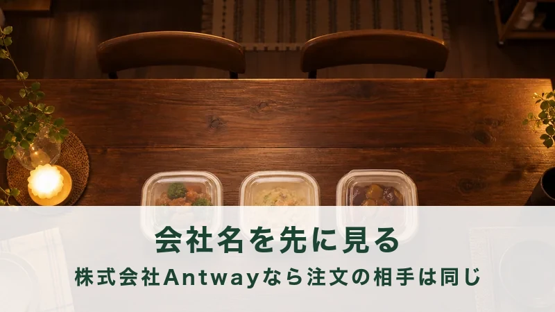 夜の食卓に並んだ惣菜の容器と、明かりの点いた台所